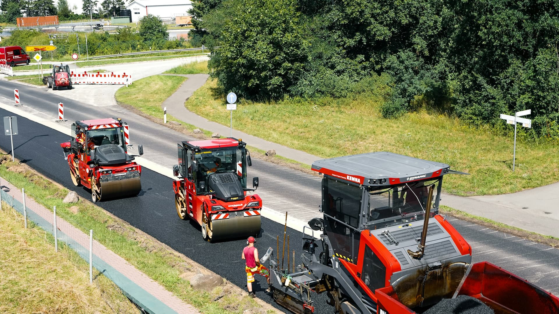 Rulli antivertici rossi e pavimentazione in lavorazione su una nuova strada asfaltata