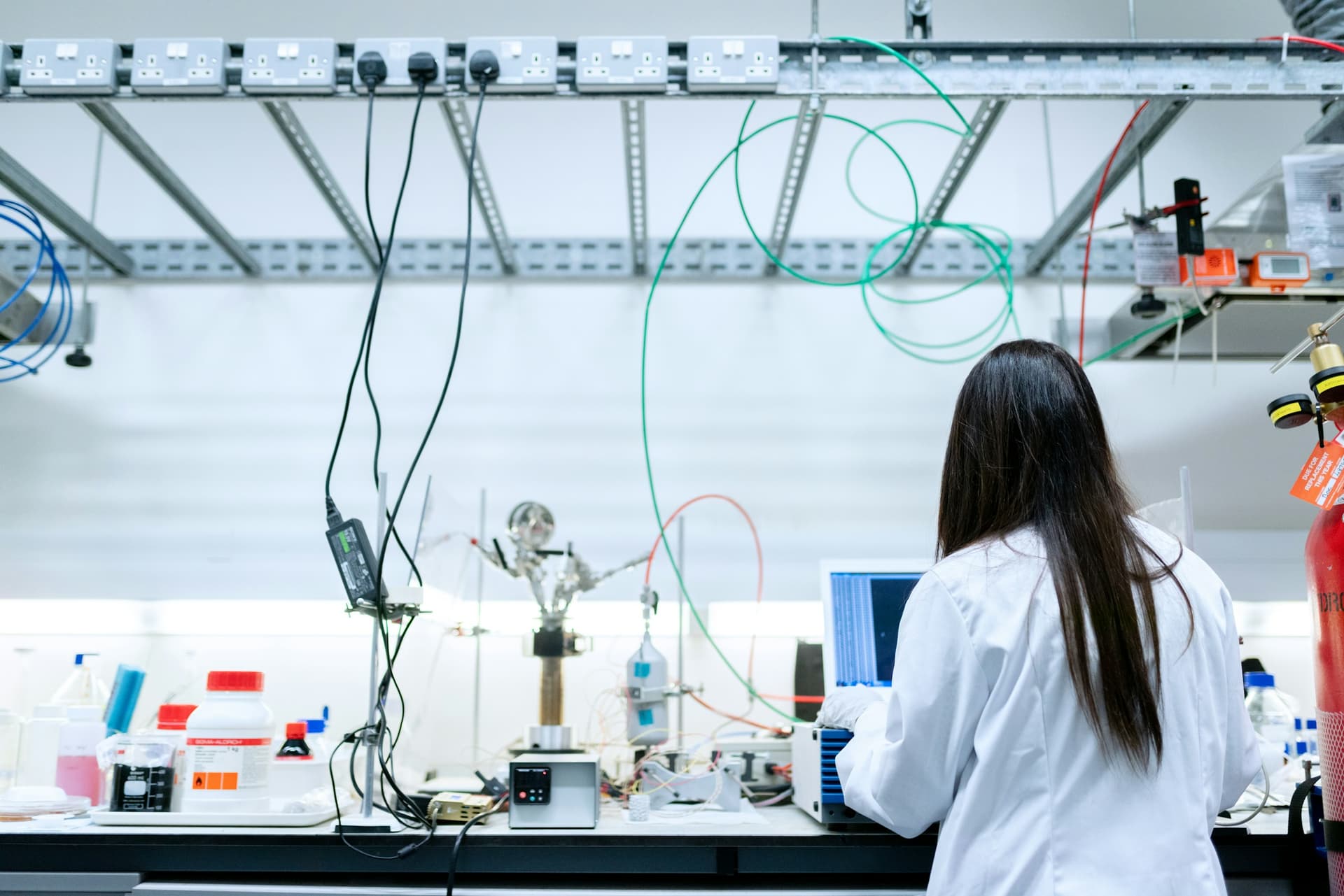 A scientist in a white lab coat working at a laptop in a laboratory