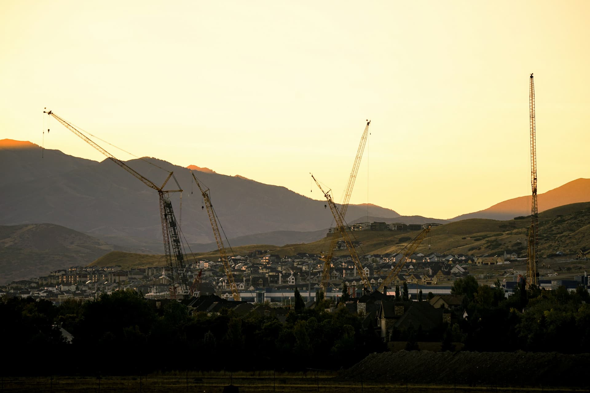 Construction cranes rising against a hazy mountain sunset